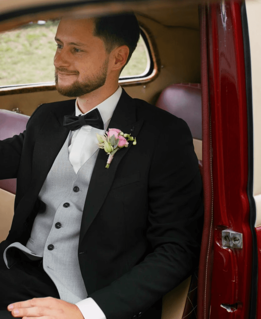 Groom in formal tuxedo with boutonniere sitting in luxury wedding car interior