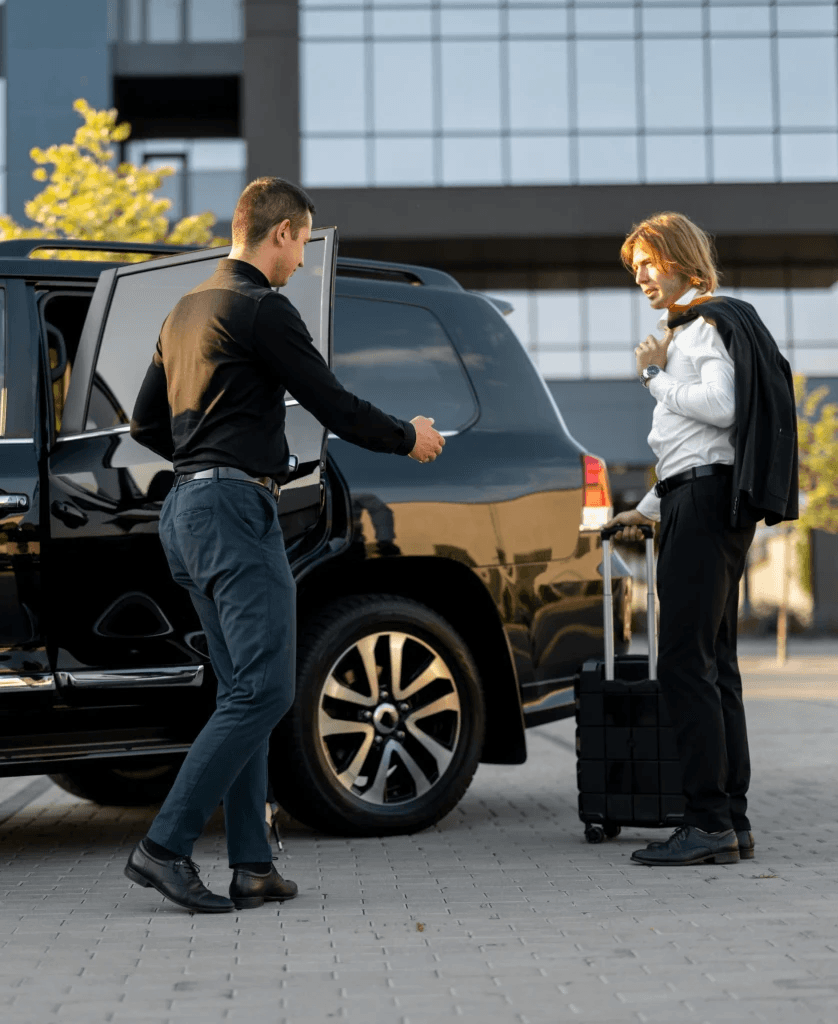 Professional chauffeur helping female passenger with luggage at luxury SUV outside modern building